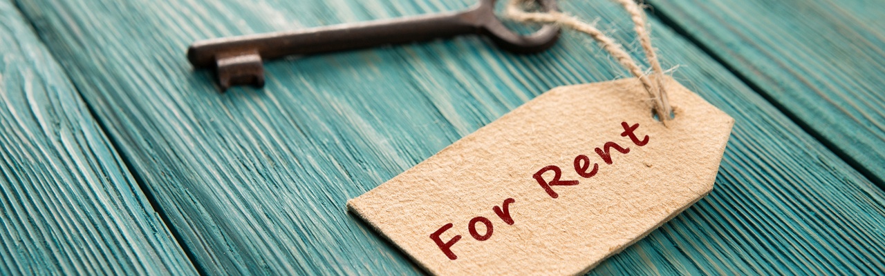 A key with a 'For Rent' tag sits on a wooden table