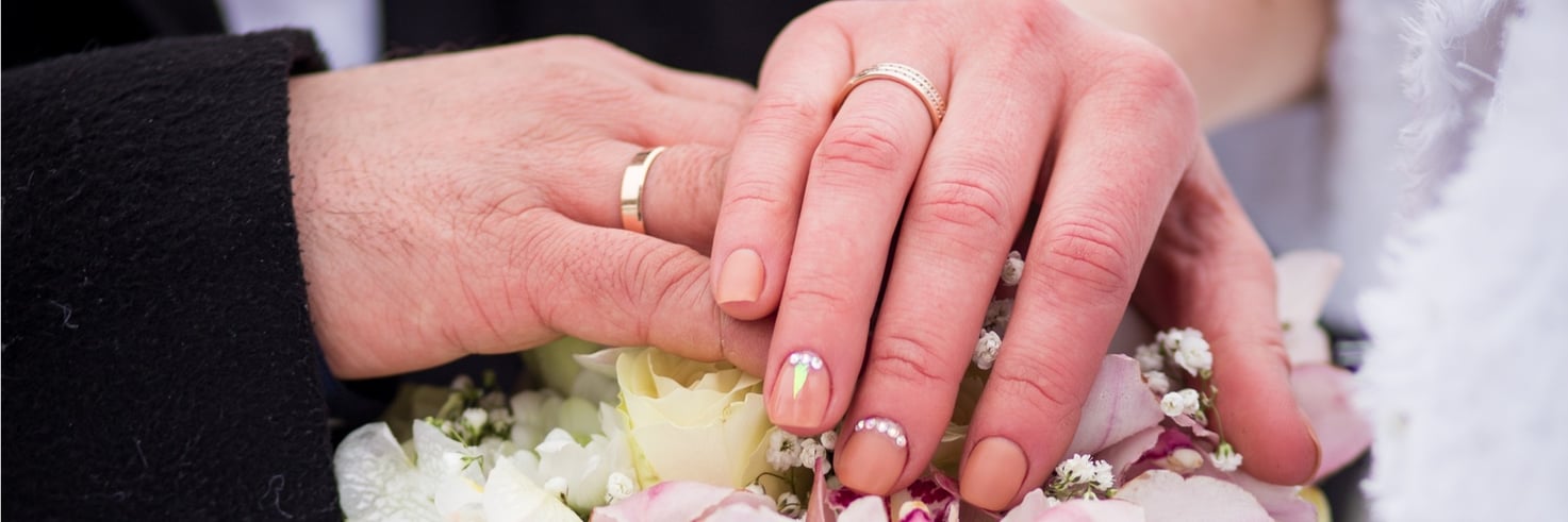 A bride and groom display their wedding bands in a traditional wedding pose